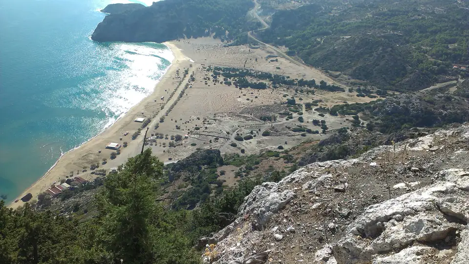 Blick von einem felsigen Berghang auf einen langen Sandstrand und blaues Meer