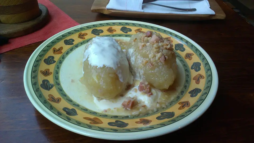Zwei längliche Kartoffelklöße mit heller Sauce und Speckstückchen auf einem bunten Teller