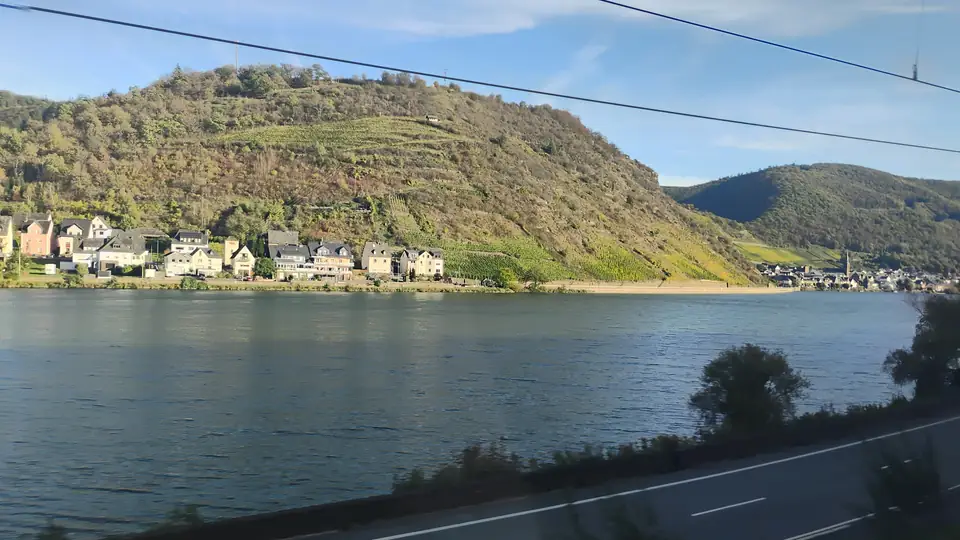 Breiter Fluss vor einem steilen Hang mit Weinbergen und einem Dorf am Ufer