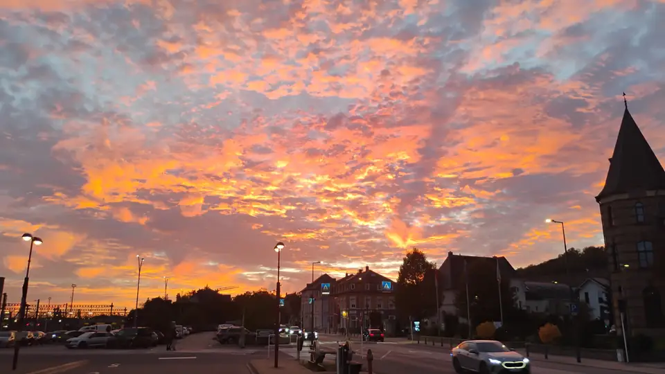 Orange und rosa leuchtende Wolken über einer Straßenkreuzung mit Häusern und einem Kirchturm