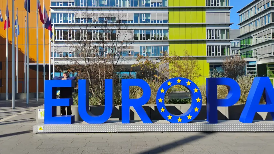 Große blaue Buchstaben EUROPA mit Sternenkranz im O vor einem Bürogebäude mit gelben und grünen Fassadenteilen