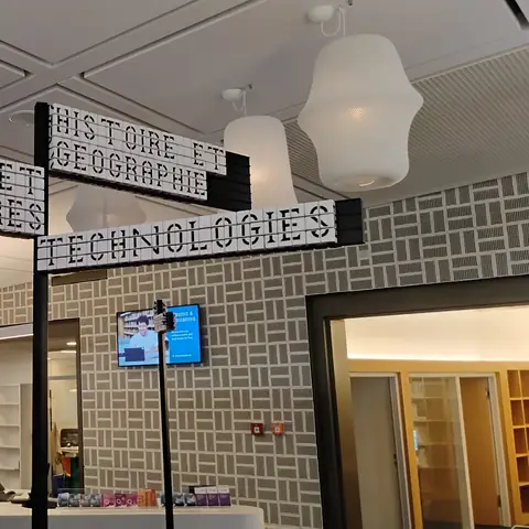 Hängende Wegweiser in Großbuchstaben mit den Aufschriften Langues et littératures, Histoire et géographie und Technologies