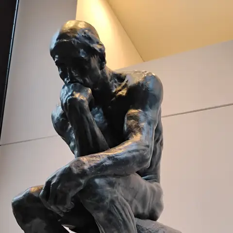 Bronzeskulptur eines sitzenden Mannes, der das Kinn nachdenklich auf die Hand stützt