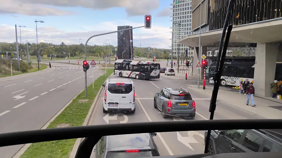 Blick durch die große Frontscheibe aus dem Oberdeck eines Busses auf eine mehrspurige Kreuzung mit Ampeln und Autos