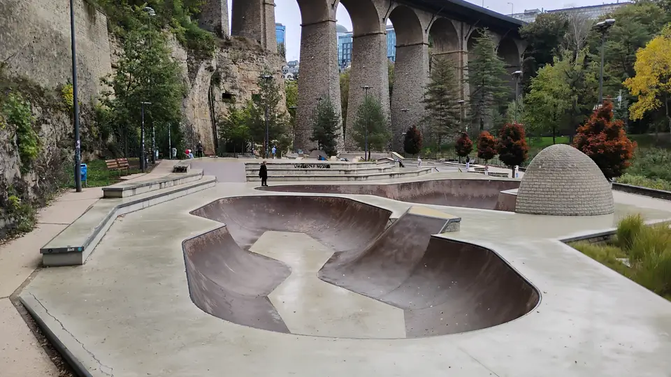 Geschwungene Betonbecken eines Skateparks im Tal, dahinter ein Viadukt mit hohen Steinbögen