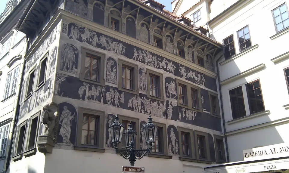 Dunkle Eckfassade mit hellen figürlichen Sgraffiti und weit vorspringendem Dach