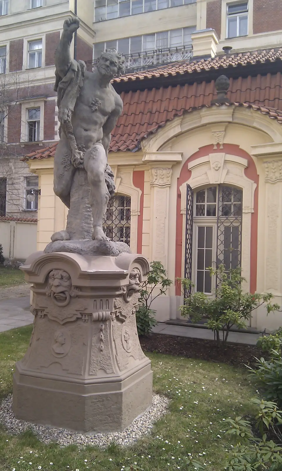 Sandsteinfigur des Riesen Cacus mit erhobenem Arm auf einem geschmückten Sockel vor einem barocken Gartenpavillon