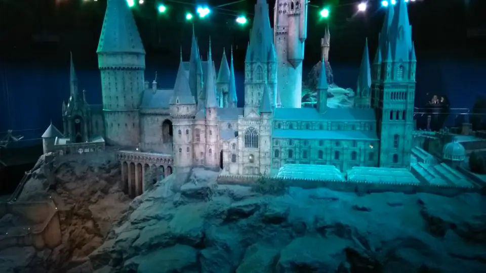 Großes Modell von Hogwarts mit zahlreichen Türmen und Gebäudeflügeln auf einem Felsen unter blauem Licht