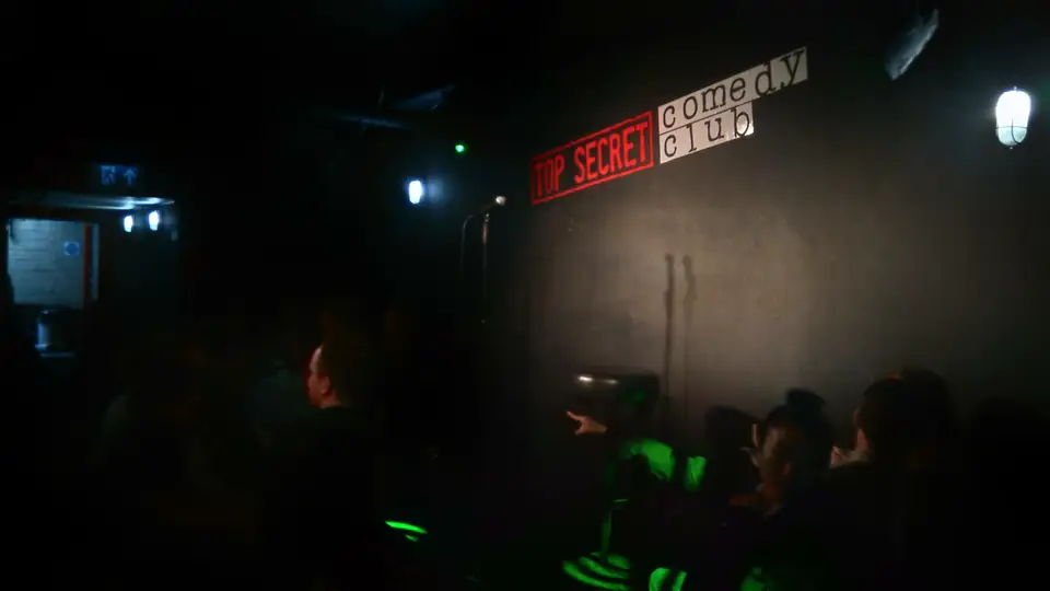 Bühne mit dunklem Vorhang und dem Logo des Top Secret Comedy Club