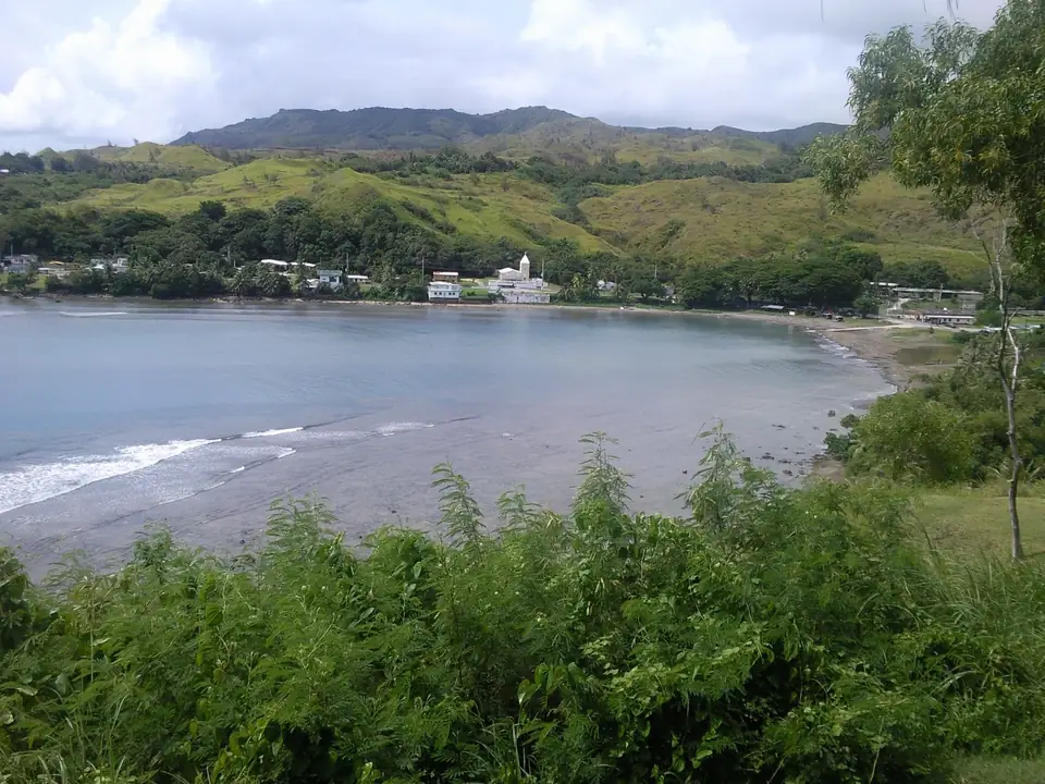 Blick von einer Anhöhe auf eine Bucht, das Dorf und grüne Hügel