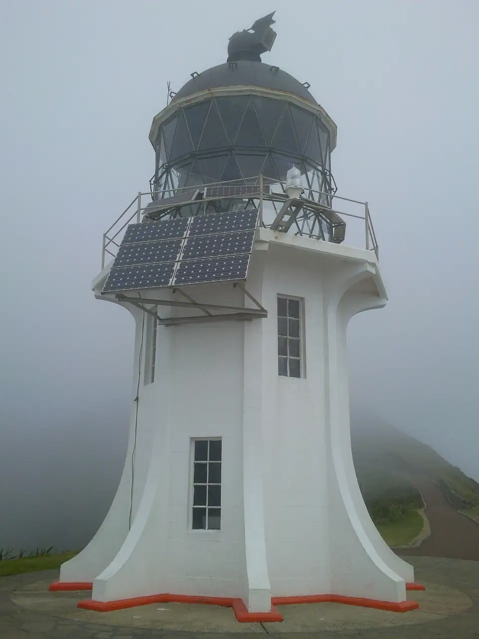 Weißer Leuchtturm mit rotem Sockel in dichtem Nebel