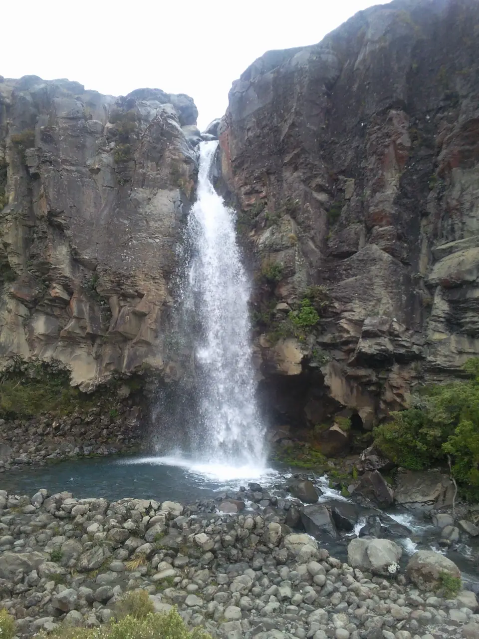Taranaki Falls vor einer steilen Lavafelswand und einem Becken mit großen Steinen