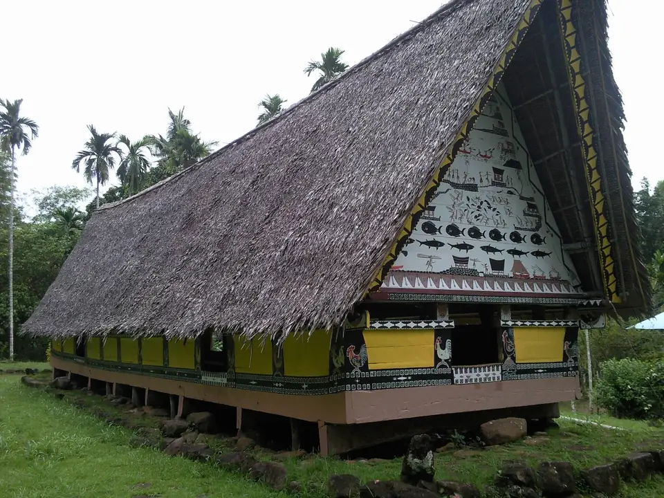 Traditionelles Versammlungshaus mit steilem, bemaltem Giebel und Palmen in Airai