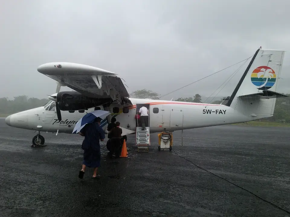 Reisende steigen bei Regen in ein zweimotoriges Propellerflugzeug von Polynesian Airlines ein