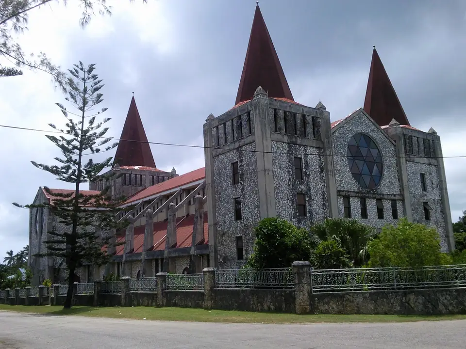 Steinerne Kirche mit roten Turmspitzen und großer runder Fensteröffnung