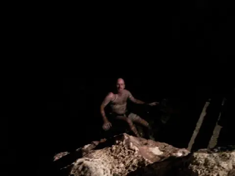 Der Reisende in Badehose am Rand eines dunklen unterirdischen Wasserbeckens